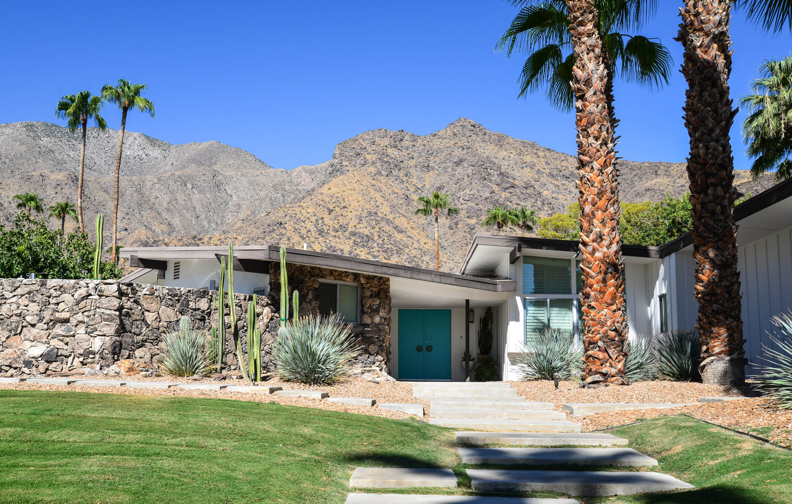 exterior of a brick home in front of mountains with a blue door painted by a painter near me